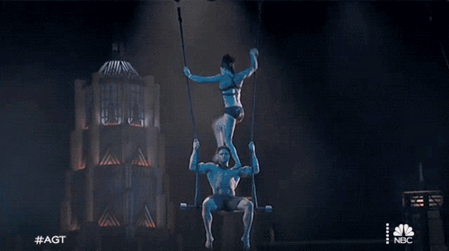 a man and a woman are hanging from a rope in front of a building with nbc written on the bottom