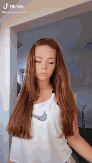 a girl with long red hair is wearing a white tank top with a nike logo on it .