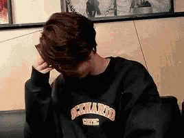 a young man wearing a black sweatshirt is sitting on a couch with his hand on his head .