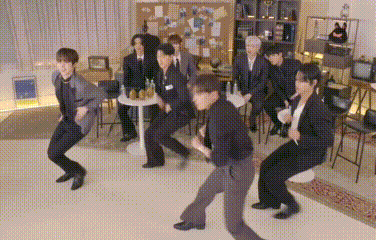 a group of people are dancing in a room while sitting at a table .