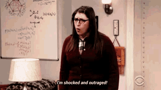 a woman wearing glasses is standing in front of a whiteboard and says `` i 'm shocked and outraged ''