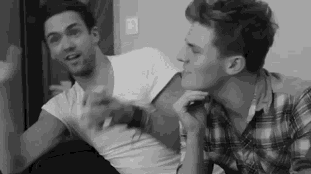 a black and white photo of two men sitting on a couch talking to each other .