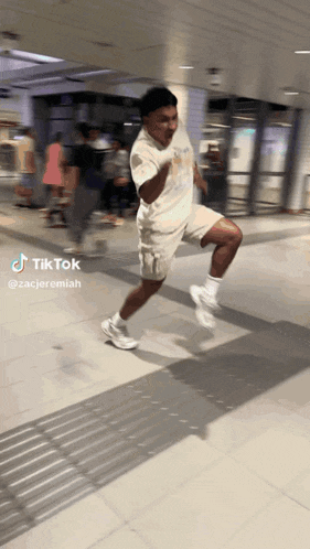 a man in a white shirt and shorts is running on a tiled floor in a tiktok video