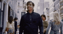 a man in a black shirt is walking down a city street with a group of people .
