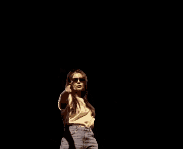 a woman wearing sunglasses and a yellow t-shirt is dancing on a black background .