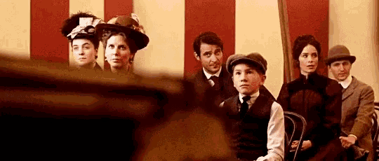 a group of people are sitting in a row in front of a red and white striped wall .