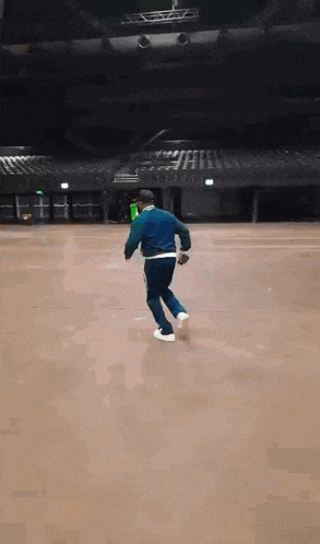 a man in a blue jacket and black pants is running in an empty arena