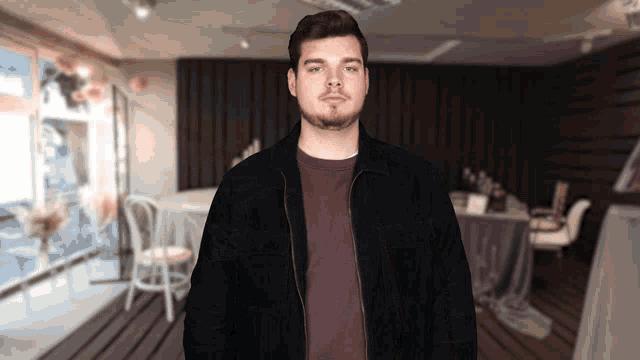 a man in a black jacket stands in a room with tables and chairs