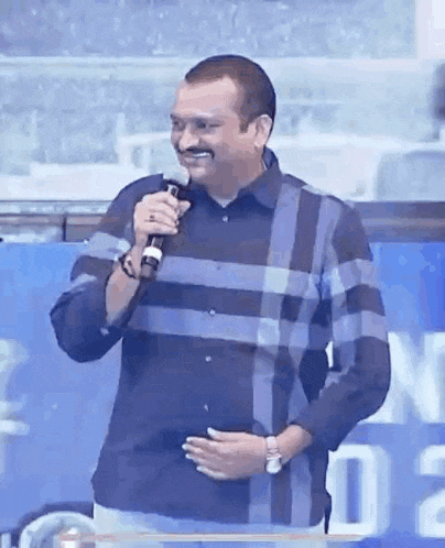 a man is holding a microphone and smiling while standing in front of a blue sign .