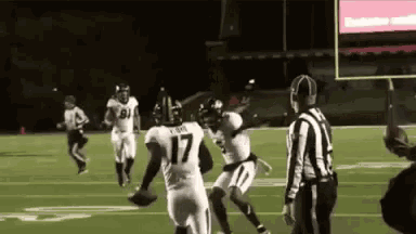 a group of football players are playing a game on a field while a referee watches .