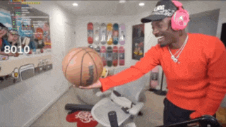 a man wearing headphones holds a basketball in a room with the number 8010 on the screen