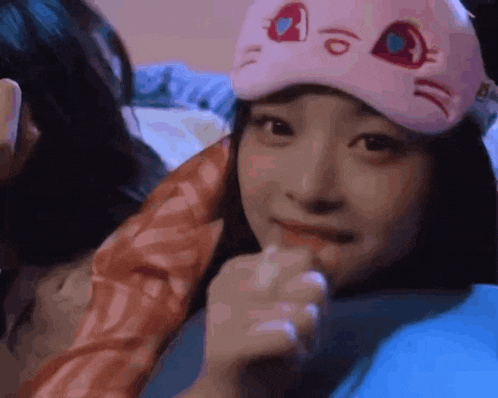 a woman wearing a pink sleep mask is sitting on a bed .