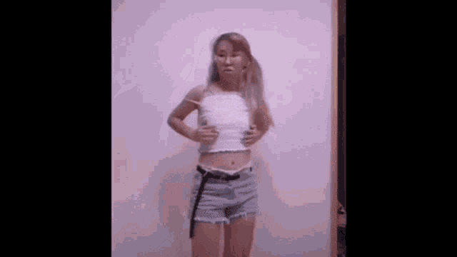 a woman in a white tank top and shorts is standing in front of a wall .