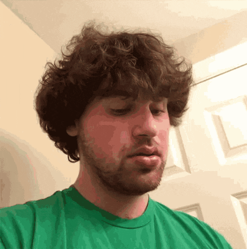 a man with curly hair and a green shirt looks down