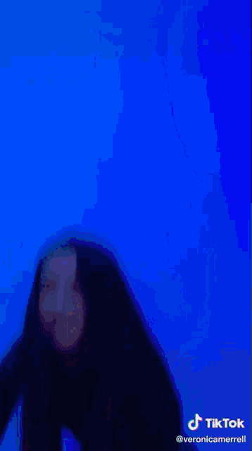 a woman wearing a black crop top and blue jeans is dancing in front of a purple background .