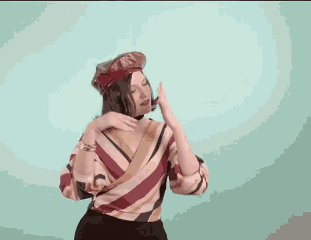 a woman wearing a beret and a striped shirt is dancing against a blue background .