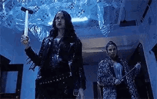a woman is holding a hammer and a knife while standing next to another woman in a room .