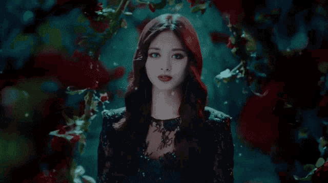 a woman with red hair and blue eyes is standing in a dark room surrounded by flowers .