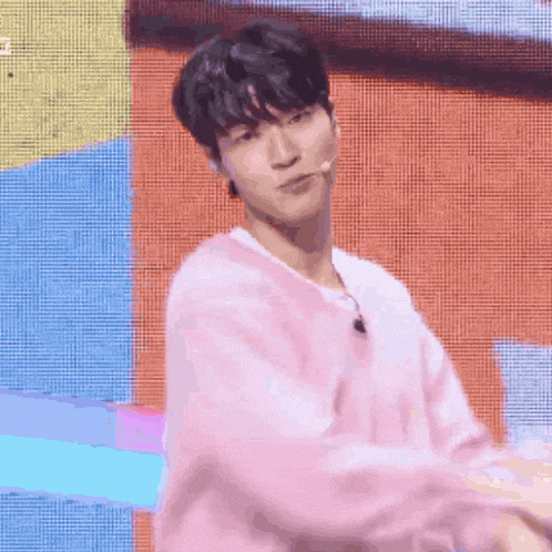 a young man in a pink sweater is dancing on a stage in front of a colorful background .
