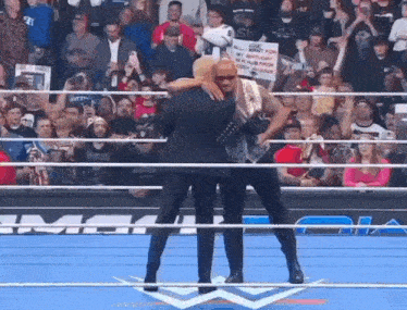 a man in a suit is hugging another man in a wrestling ring in front of a crowd .