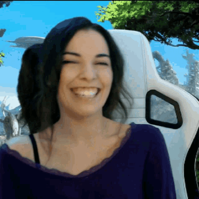 a woman in a purple shirt is smiling in front of a white chair