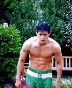 a shirtless man in green shorts is standing in front of a bench in a garden .
