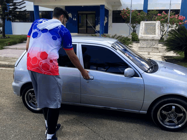 a man in a red white and blue shirt is opening a silver car door