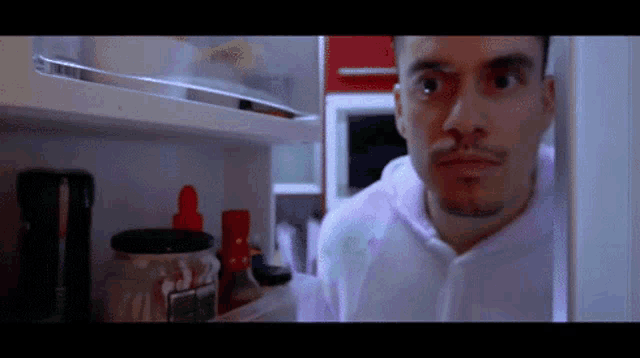 a man looking into a refrigerator with a jar of ketchup in it