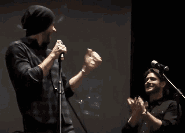 two men singing into microphones on a stage