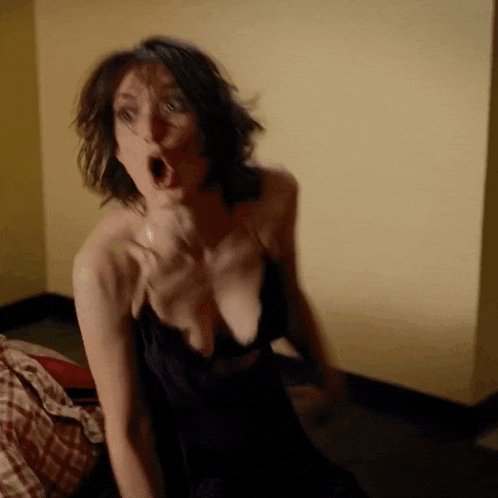 a woman in a black dress is sitting on the floor with her mouth open and a surprised look on her face .