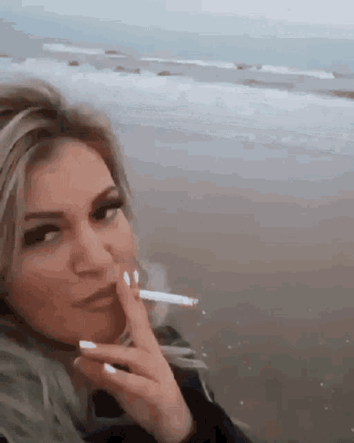 a woman is smoking a cigarette at the beach .