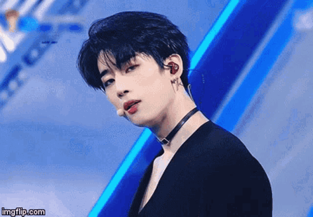 a young man wearing a choker and ear buds is standing in front of a blue background .