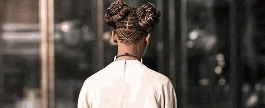 a woman with braids and a shaved nape is standing in front of a glass building .