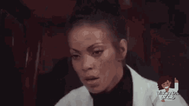 a woman in a white lab coat and black turtleneck is sitting in a chair .