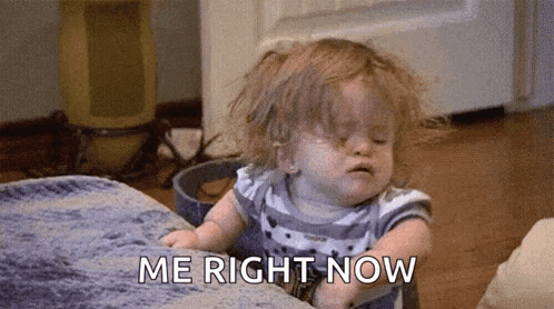 a baby girl is sitting on a bed with her eyes closed and the words `` me right now '' written on the floor .