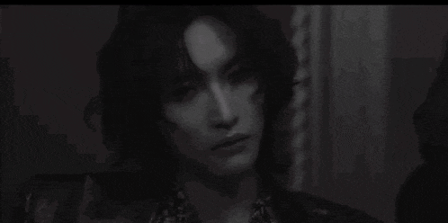 a black and white photo of a young man with long hair in a room .