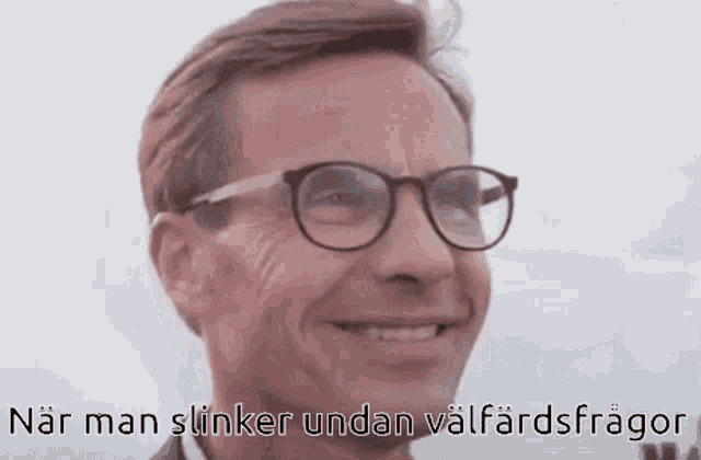 a man wearing glasses is smiling and looking at the camera with a caption in a foreign language .