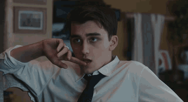 a young man in a white shirt and black tie smoking a cigarette