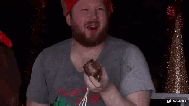 a man with a beard wearing a santa hat is eating a donut .