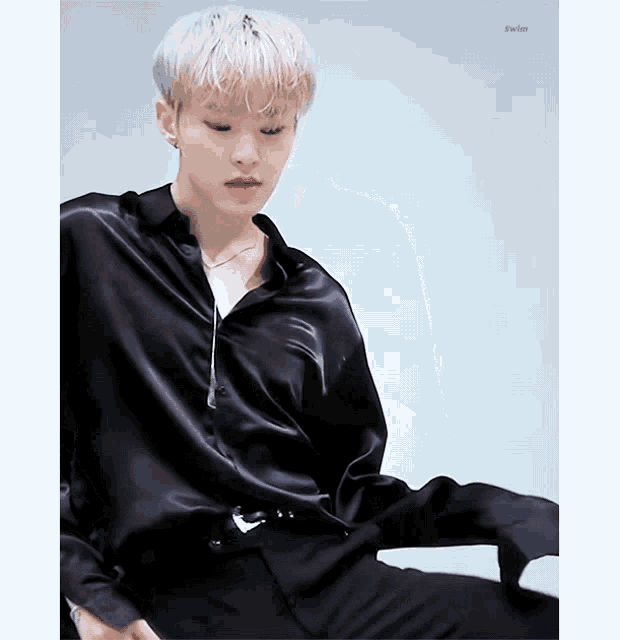 a young man wearing a black satin shirt and black pants is sitting down