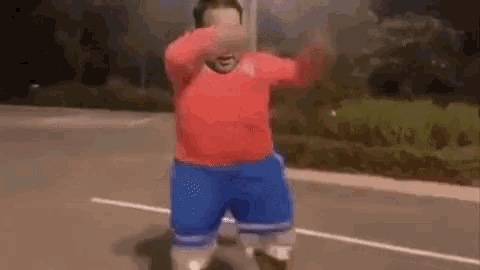 a man in a red sweater and blue shorts is dancing on a basketball court at night .