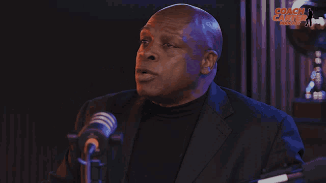 a man in a suit speaking into a microphone with the words coach carter podcast behind him
