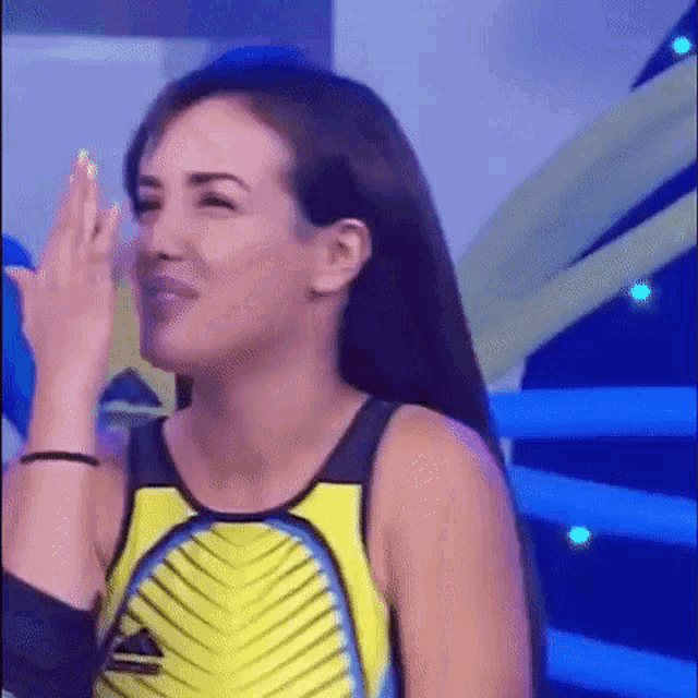 a woman in a yellow and black tank top is making a funny face and covering her face with her hand .