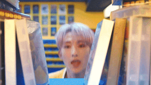 a man is peeking out from behind a pile of books in a library .
