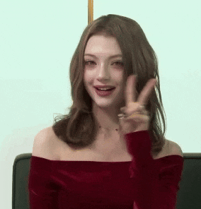 a woman wearing a red off the shoulder top is giving a peace sign .