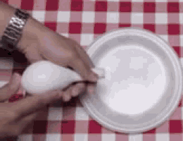 a person is holding a white spoon in front of a white plate on a checkered table cloth .