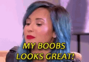 a woman with blue hair is sitting on a couch with the words `` my boobs looks great '' written on her face .