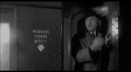 a man in a suit and tie is standing next to a sign that says `` watch your step '' .