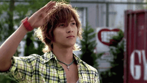 a young man wearing a plaid shirt salutes in front of a sign that says g.