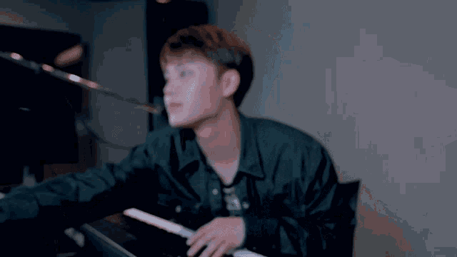 a man in a black jacket is playing a keyboard in front of a microphone